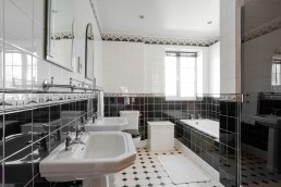 Bathroom with black and white tiles and art deco. Double sink and mirrors with a bath and shower. Location hire for TV and filming in Park Lodge, London