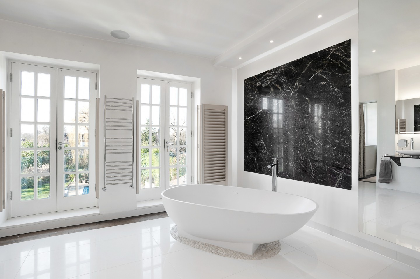 White modern bathroom with a garden view, marble decor, shutters, bathtub and good lighting. Location hire for TV and filming in Park Lodge, London