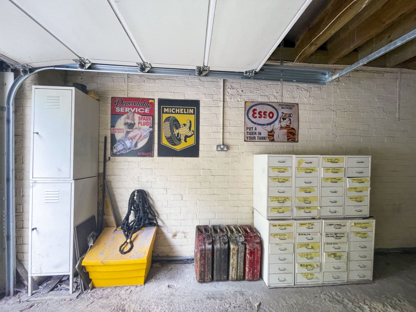 Spacious light garage with drawers and storage for bicycles, tool box and cars. Metal car posters on the wall and road signs. Location hire for TV and filming in Park Lodge, London