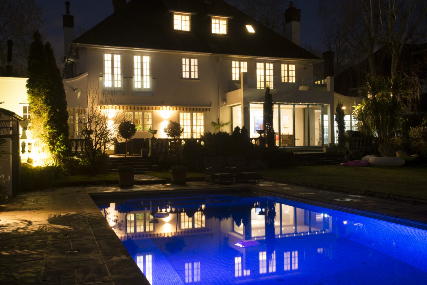 Garden at night with planters, swimming pool, trees flowers and outdoor furniture. Location hire for TV and filming in Park Lodge, London