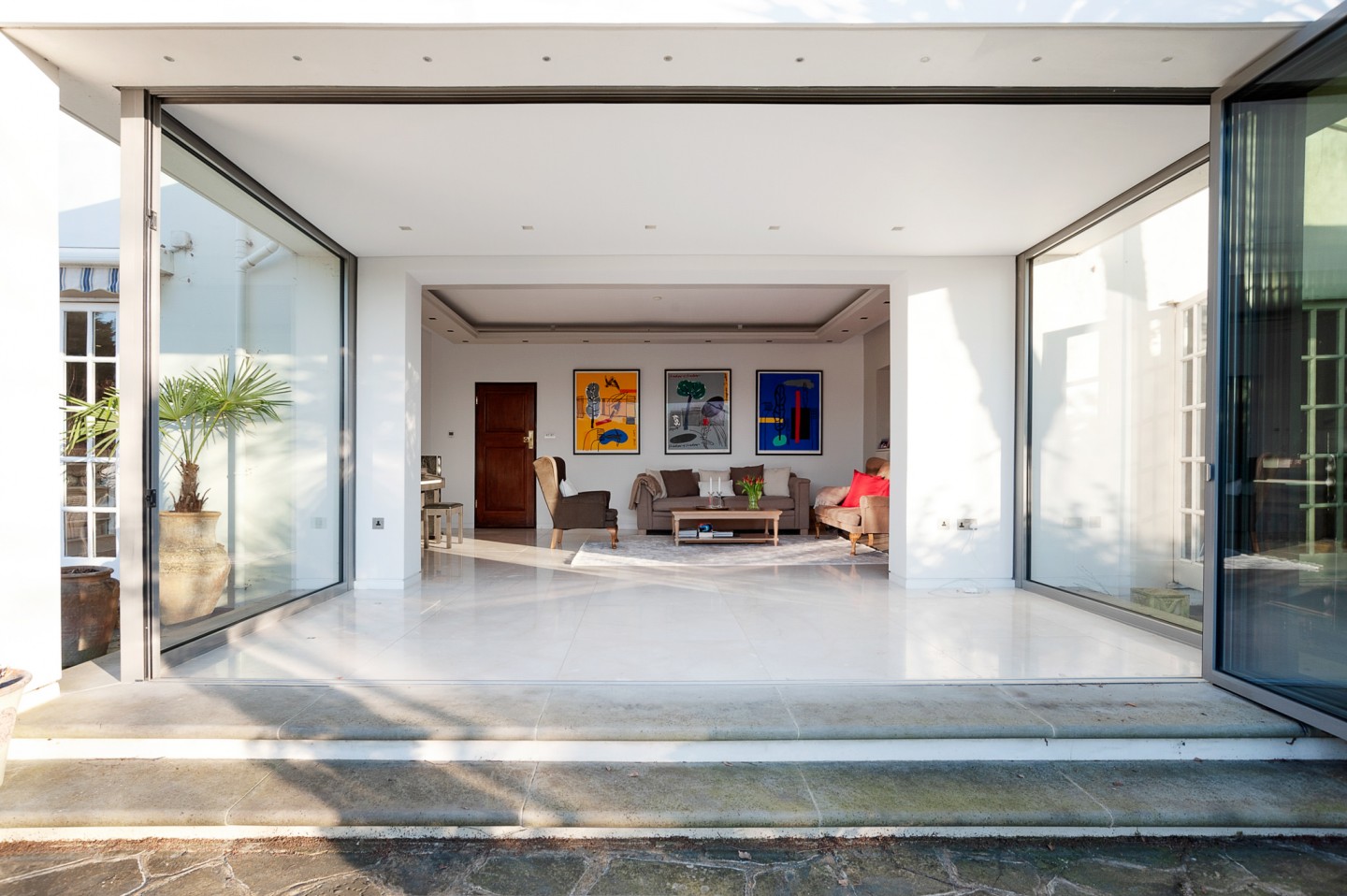 Large sitting room with art on wall, oak desk and marble floor with bifold glass window. Location hire for TV and filming in Park Lodge, London