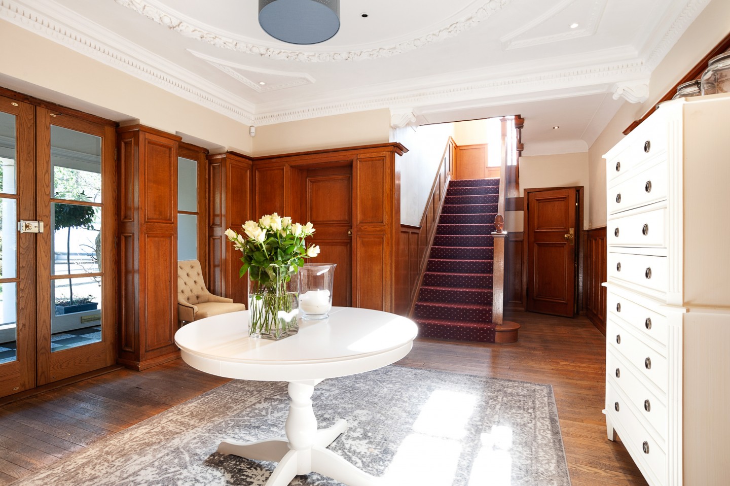 Luxurious entrance hall with large staircase and centrepiece table on oak flooring. Location hire for TV and filming in Park Lodge, London