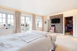 Master bedroom modern style cream sofa and double bed with bedsides and a terrace overlooking the garden. Location hire for TV and filming in Park Lodge, London