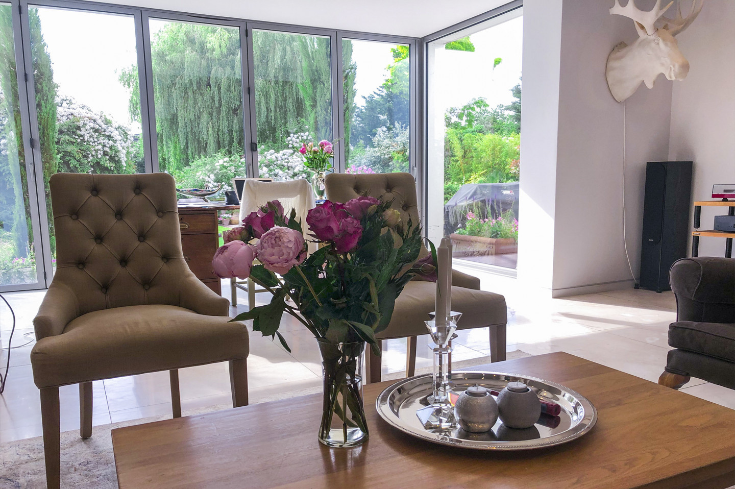 Sitting room with glass doors and marble floor. Flower centrepiece on coffee table and armchair. Location hire for TV and filming in Park Lodge, London